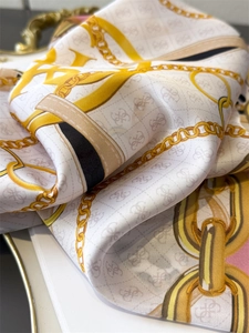 Close-up of silk-like scarf featuring interlocking logo pattern and gold chain print details