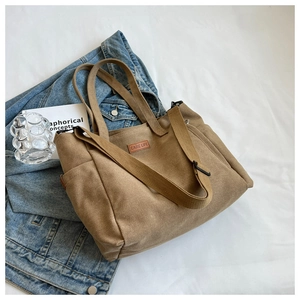 Detail of khaki canvas tote bag featuring side pockets and signature leather label