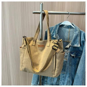 Detail of khaki canvas tote bag featuring leather brand patch and adjustable wide strap