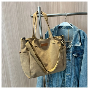 Detail view of khaki canvas tote bag with wide strap and side pocket hanging on hanger
