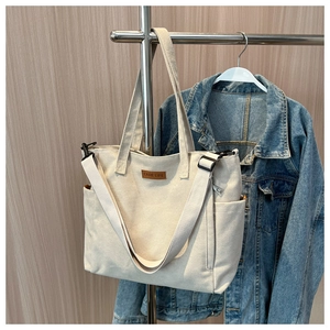 Minimalist beige canvas tote bag with side pocket and adjustable shoulder strap