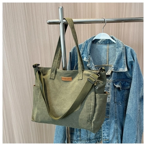 Detail of army green canvas tote bag with leather logo tag and adjustable shoulder strap