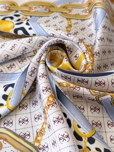 Macro detail of silk-like scarf featuring chain print and luxury logo patterns