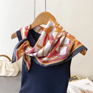 Detail of silk scarf with vintage gold chain and red bow print tied on a blue vest