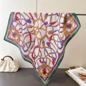 Detail of silk square scarf with golden chains and tassels hanging by a white cloud bag