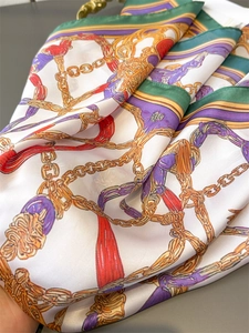 Macro detail of silk-like scarf featuring vintage gold chain print and tassel motifs