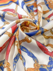 Macro shot of silk satin scarf featuring vintage gold chain and nautical rope patterns