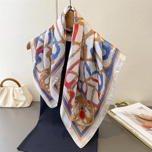 Classic chain print silk square scarf with gold rope and gemstone patterns hanging on a hanger