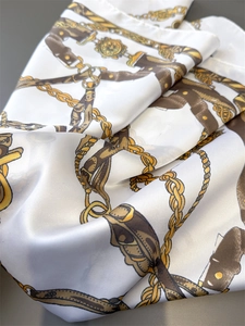 Close-up of white silk scarf showing vintage equestrian patterns and golden chain details