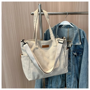 Minimalist off-white canvas tote bag with brown leather label and adjustable shoulder strap