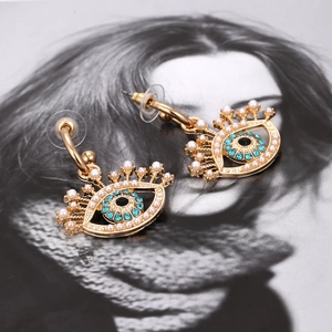 Boucles d'oreilles œil protecteur dorées avec strass bleus et perles blanches sur fond mode