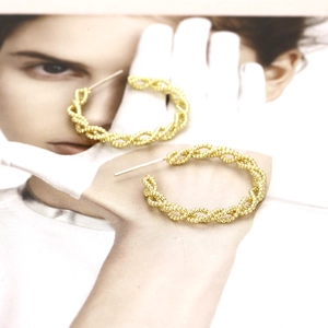 Macro shot of gold twisted hoop earrings with intricate beaded spiral texture on a card