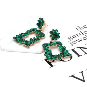 Macro detail of vintage gold floral earrings featuring emerald green crystal settings