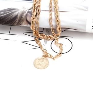 Detail of layered gold coin necklace with vintage portrait pendant on stylish magazine