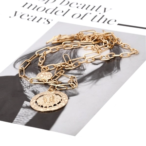 Golden paperclip chain necklace with lion head and hammered disc pendants on a magazine