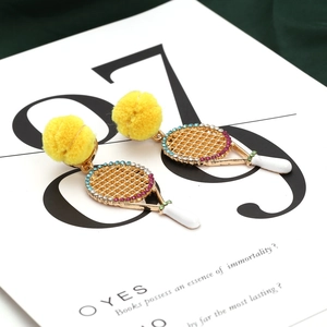 Détail macro de boucles d'oreilles raquette de tennis avec pompons jaunes et strass brillants