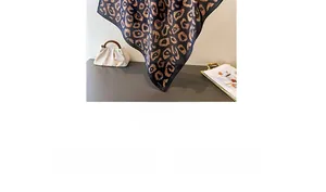 Detailed view of black leopard print silk scarf with satin texture on a white handbag
