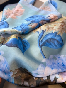 Close-up of floral print silk-like scarf featuring soft light blue fabric and rolled edges