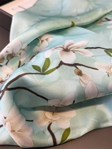 Close-up of silk scarf fabric showing elegant white magnolia prints on mint green background