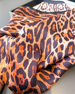 Macro shot of silk scarf fabric showing smooth leopard print texture and black hemmed edge
