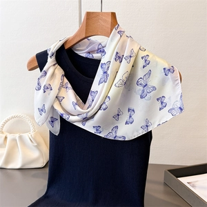 Detail of a silky butterfly print square scarf styled on a black sleeveless top with pearls