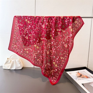Détail d'un foulard en soie bordeaux à fleurs drapé près d'un sac à main en perles blanches
