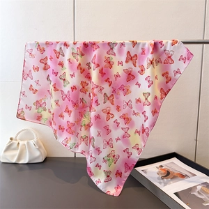 Elegant pink gradient silk scarf featuring colorful butterfly prints hanging on a metal rod