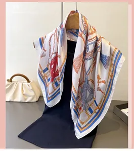 Détail d'un foulard en soie avec motifs de chaînes et pompons sur un cintre en bois