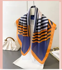 Detail of geometric stripe silk scarf hanging on a white hanger with a leather handbag
