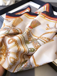 Vue détaillée d'un foulard en soie avec chaînes dorées, pompons orange et bords roulés fins