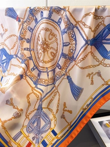 Détail d'un foulard en soie avec motifs de chaînes dorées et bordures bleu marine
