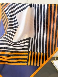 Detailed view of geometric striped silk-like scarf with orange rolled edges and patterns