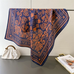 Detailansicht eines floral bedruckten Seidenquadrats in Marineblau und Orange auf einem Ständer