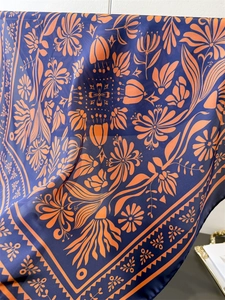 Detail eines Seidenschals mit orangefarbenem Blumenmuster auf dunkelblauem Stoff mit Rollsaum