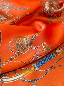 Detailaufnahme von orangefarbenem Seidenschal mit Kutschenmuster und glänzendem Tuchring
