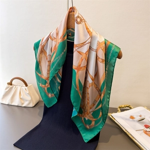 Elegant emerald and orange equestrian print silk scarf draped over a black mannequin top