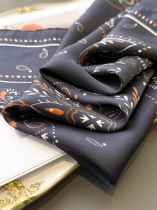 Detailed shot of dark paisley silk scarf with orange floral patterns on a vintage tray