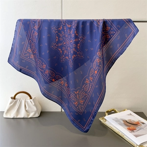 Detail of blue silk-like square scarf with paisley floral print hanging near a handbag