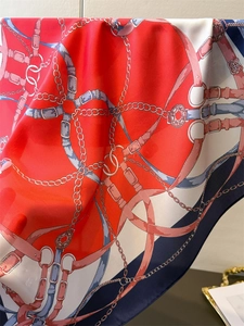 Detail of silk scarf showing vibrant red and blue equestrian print with chain patterns