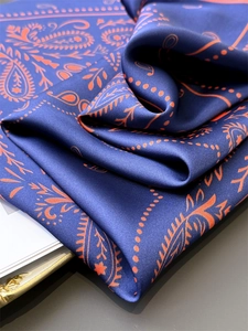Detailed view of paisley silk scarf with royal blue satin texture and orange patterns