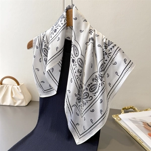 Elegant white satin square scarf with black paisley pattern on a blue sweater