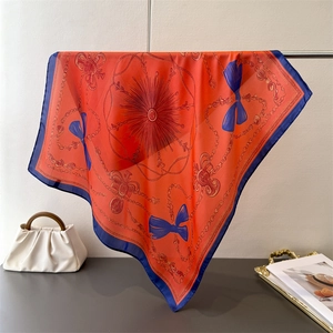 Detail of silk scarf with orange chain print and blue borders on a display stand
