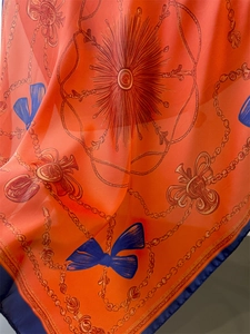 Detailed texture of vibrant orange silk scarf featuring gold chain and bow patterns