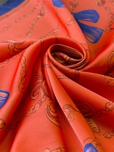 Detail of silk scarf with gold chain and tassel print over vibrant coral orange fabric