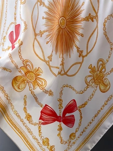 Detail of silk scarf with chain print, sunburst patterns, and red bow accents on ivory base