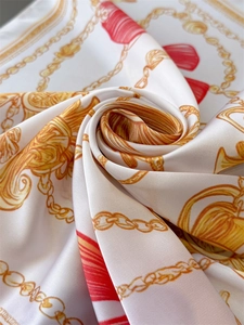 Detailed close-up of luxurious silk scarf with golden chain and red tassel print