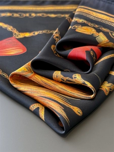 Close-up of silk scarf showing luxury gold chain print and red bow on black satin