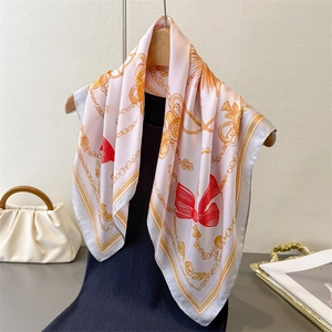Pink silk square scarf with vintage gold chains and red bow patterns hung on a hanger