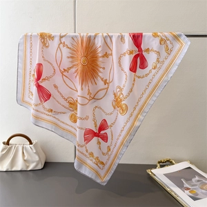 Detail of silk square scarf featuring golden chain prints and red bow motifs