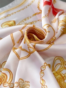 Macro shot of silk scarf with gold chain and red bow print showing soft fabric folds